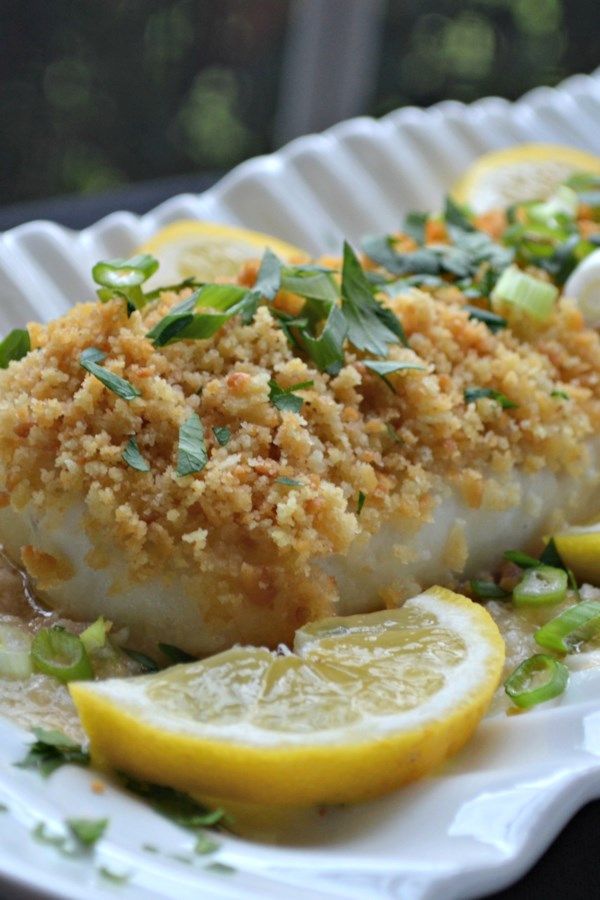 a white plate topped with fish covered in sauce and garnished with lemon slices