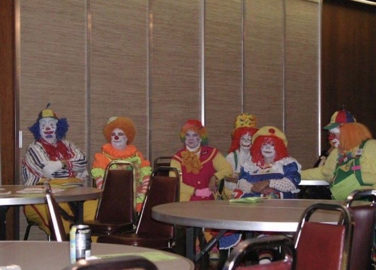 several clowns are sitting at round tables in a room with blinds on the wall