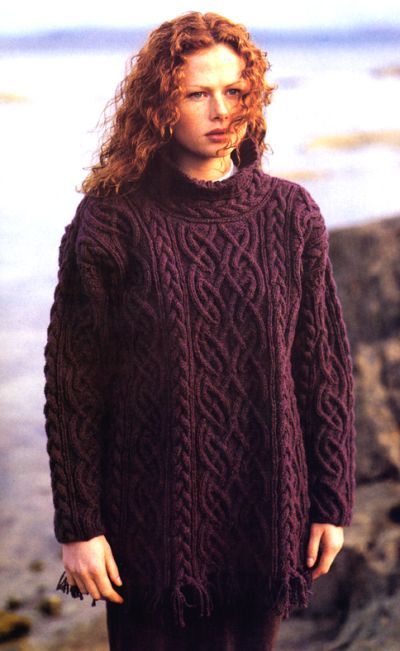 a woman standing on the beach wearing a purple sweater