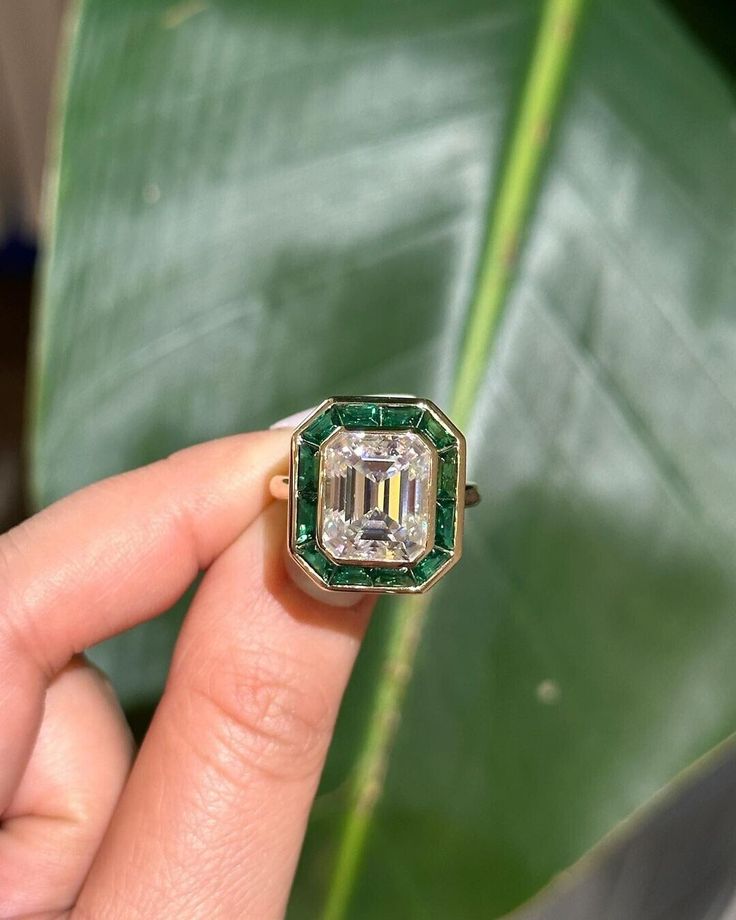 a woman's hand holding a ring with an emerald center surrounded by white diamonds