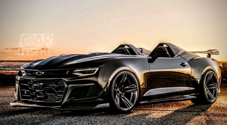 a black chevrolet camaro is parked on the side of the road with sunset in the background