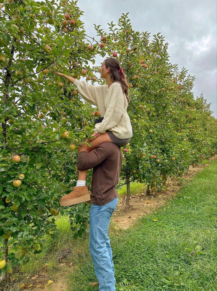 a man carrying a woman on his back in an apple orchard