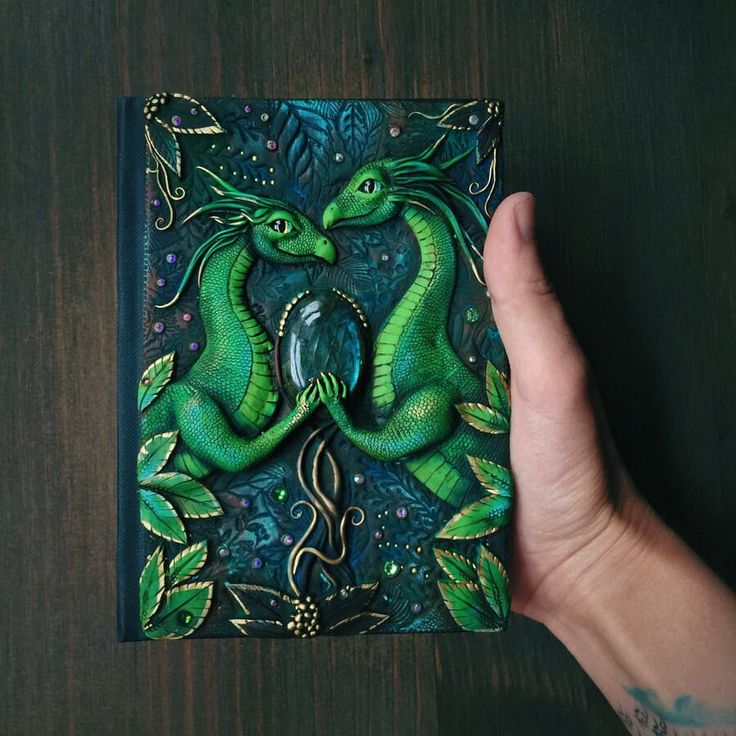 a hand holding a green dragon book on top of a wooden table