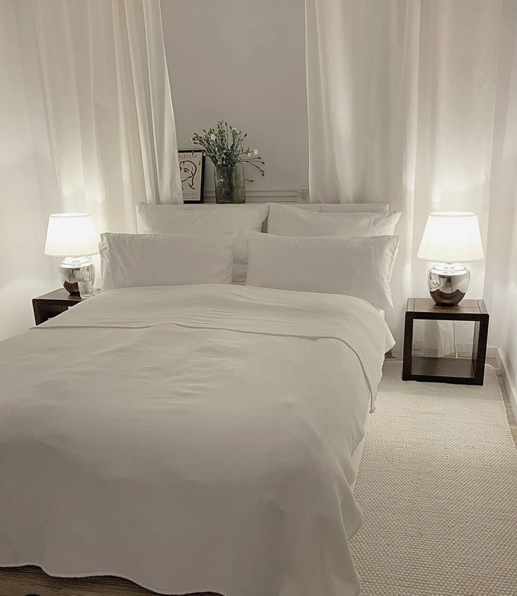 a bed with white sheets and pillows in a bedroom next to two lamps on either side of the bed