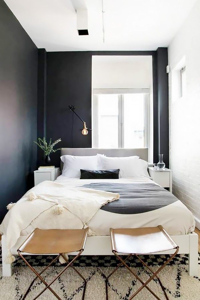 a bedroom with black walls, white bedding and two stools in front of the bed