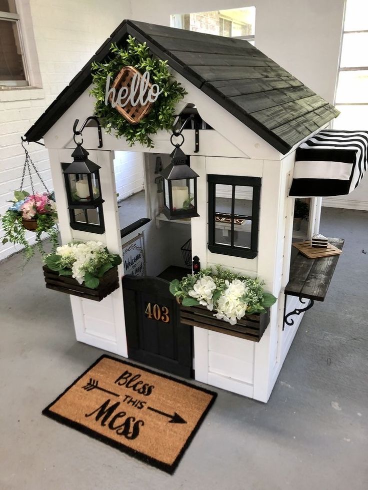 a house shaped like a doghouse with flowers in the window boxes and welcome mat on the floor