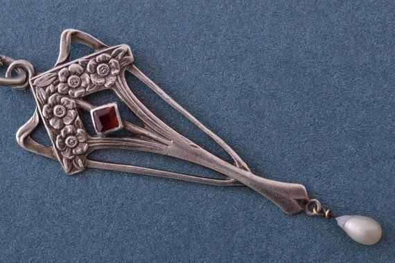 a silver necklace with an ornate design and garnishes on the side, hanging from a chain