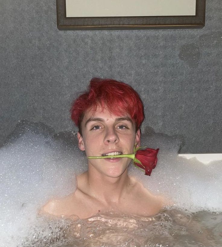 a man with red hair is in the bathtub holding a flower to his mouth