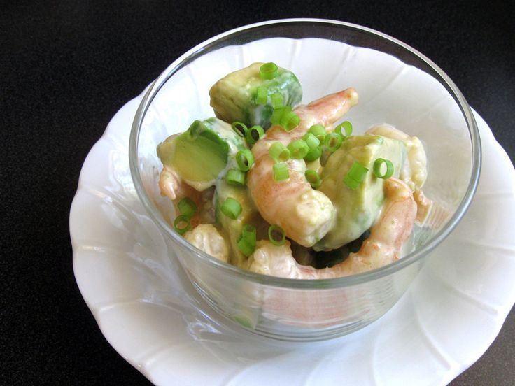 a bowl filled with shrimp and vegetables on top of a white plate next to a black table