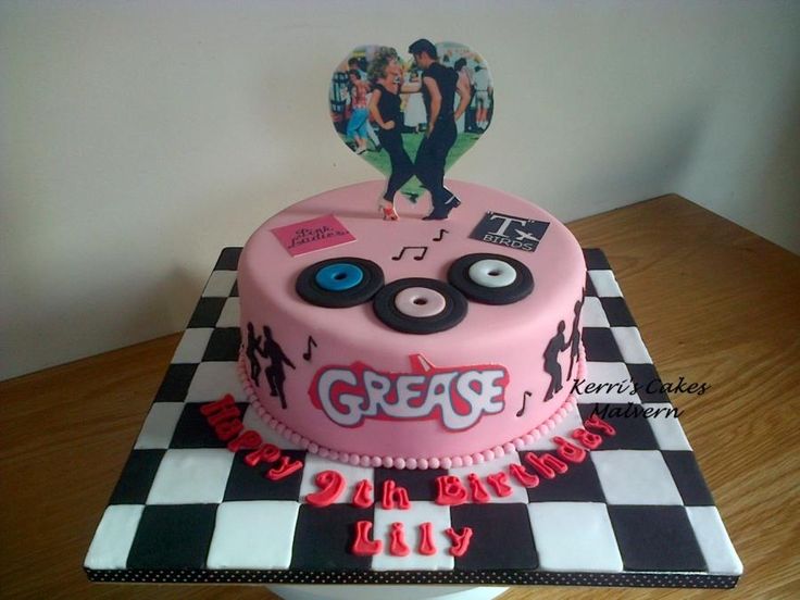 a pink cake with music themed decorations on it's top and the words grease