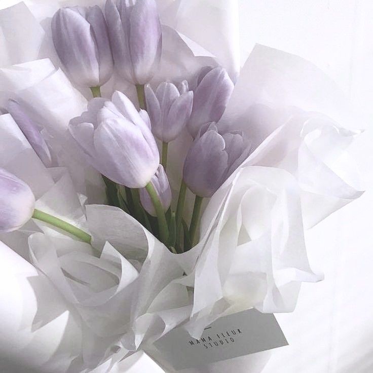 a bouquet of purple tulips sitting on top of a white cloth covered table