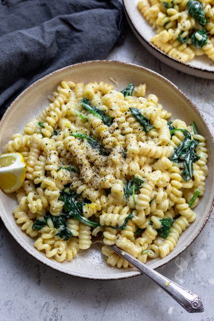 two plates filled with pasta and spinach on top of a marble table next to a black towel