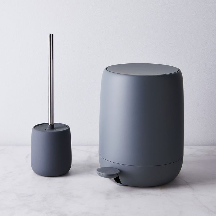 a grey toilet brush holder next to a gray cup on a white countertop with a black handle