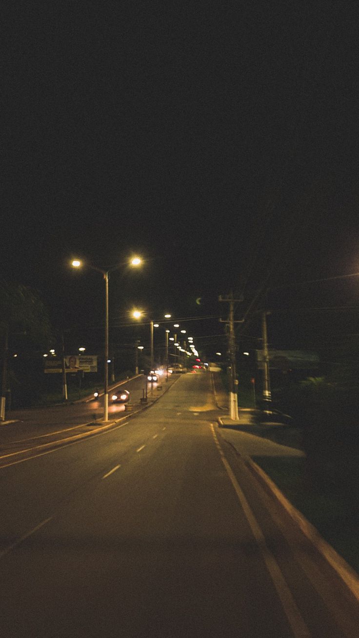 an empty street at night with cars driving down it