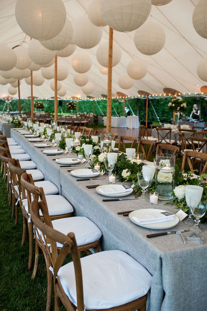 a long table is set with white plates and place settings for an outdoor wedding reception