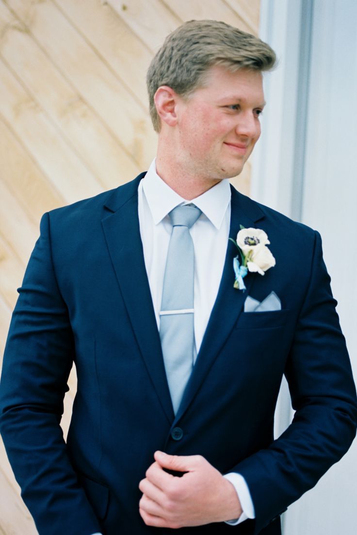 a man in a suit and tie standing next to a wooden wall wearing a boutonniere