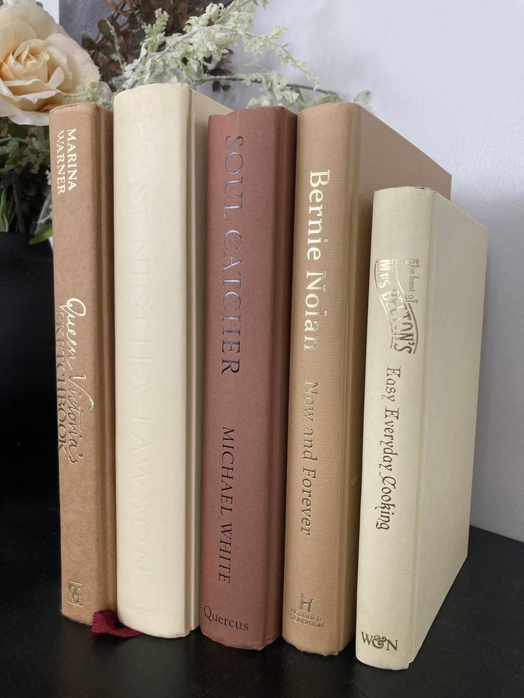 three books sitting on top of a table next to a vase with flowers in it