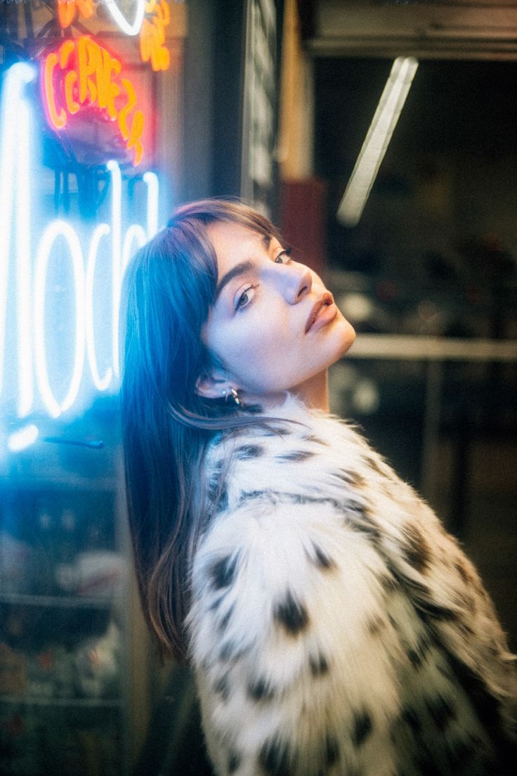 a woman standing in front of a neon sign with her hair blowing in the wind