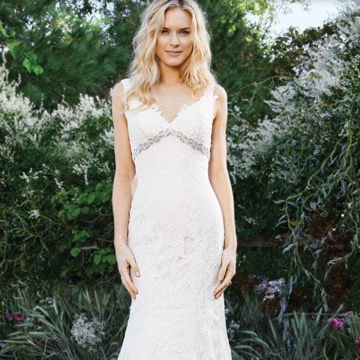 a woman in a white wedding dress standing next to bushes and flowers with her hands on her hips