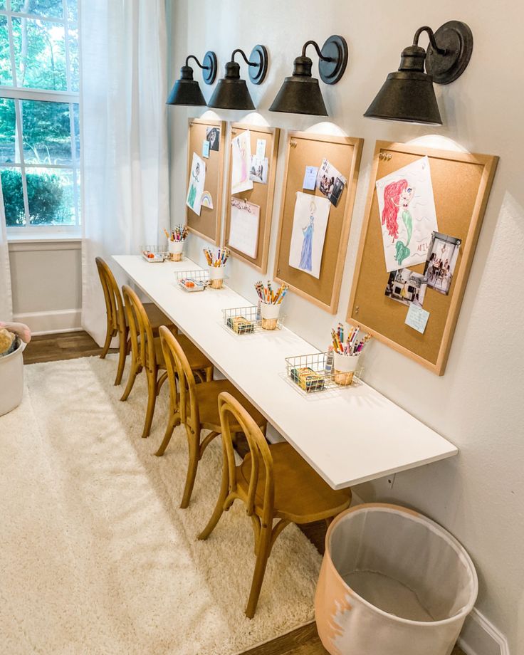 a room with several pictures on the wall and wooden chairs in front of two windows