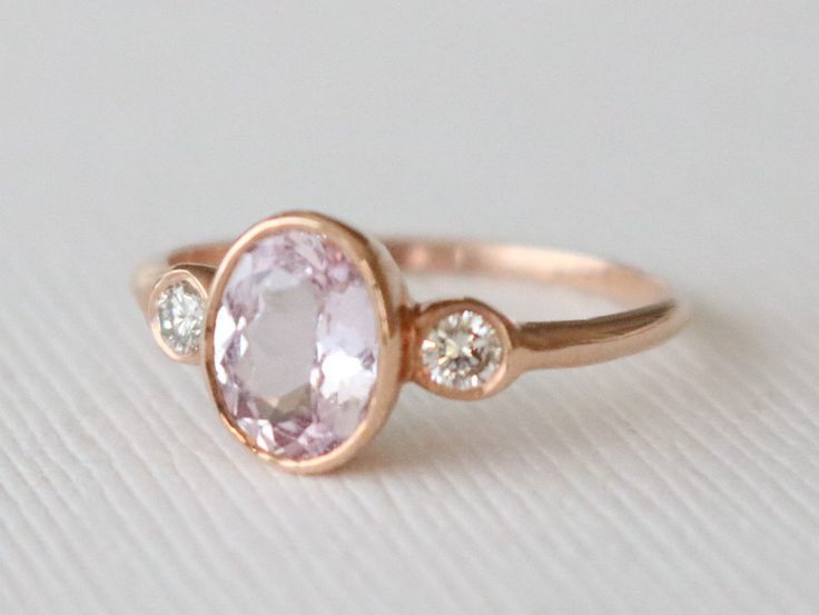 a close up of a ring with an oval shaped pink stone and two small diamonds