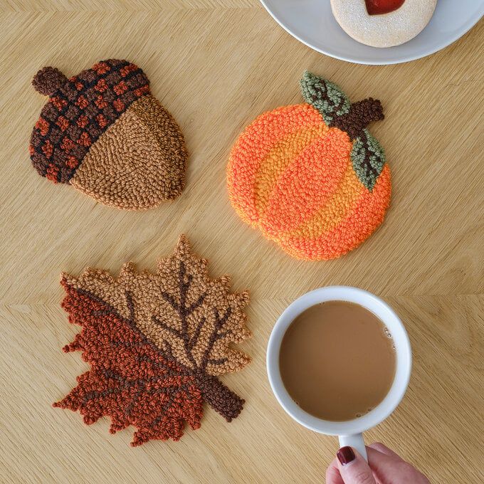 a person is holding a coffee cup in front of two knitted coasters with leaves and acorns on them