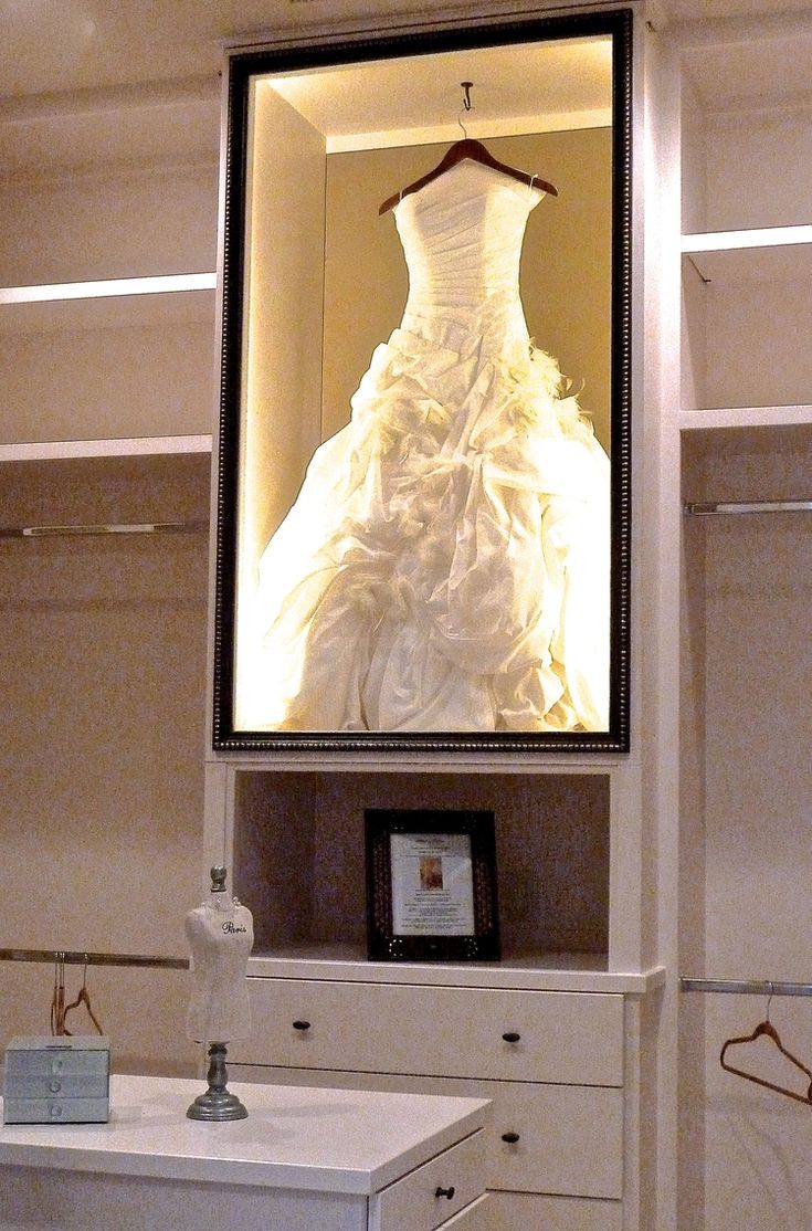 a wedding dress is on display in a mirror above a dresser with clothes hanging from it