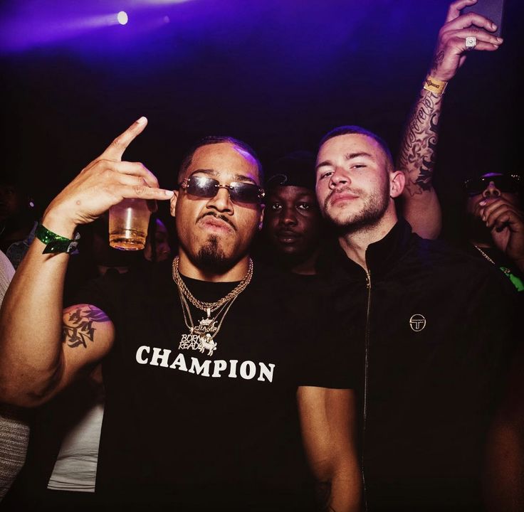 two men standing next to each other in front of a crowd at a nightclub holding up their fingers