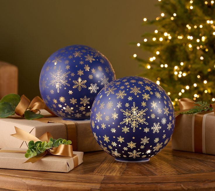 two blue balls decorated with snowflakes sit on a table next to presents and a christmas tree