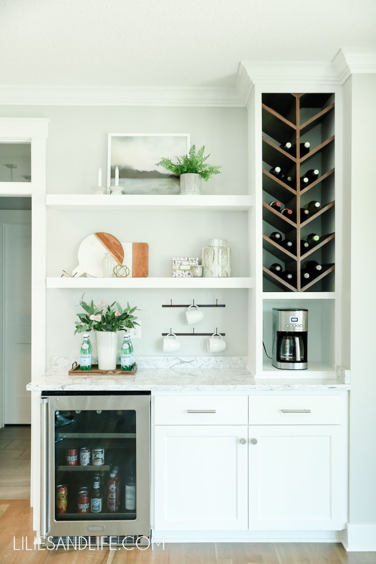 a kitchen with white cabinets and shelves filled with wine bottles, coffee cups, and other items