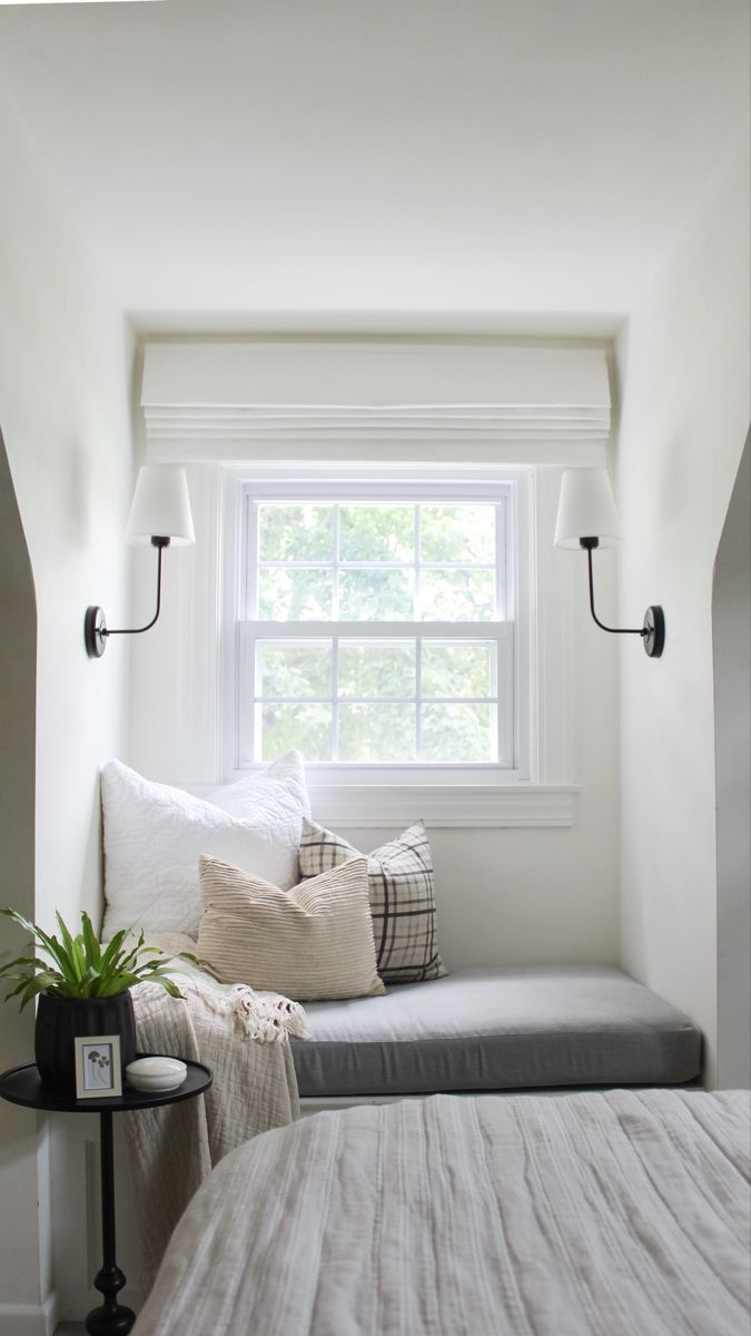 a bed sitting under a window next to a small table with a potted plant