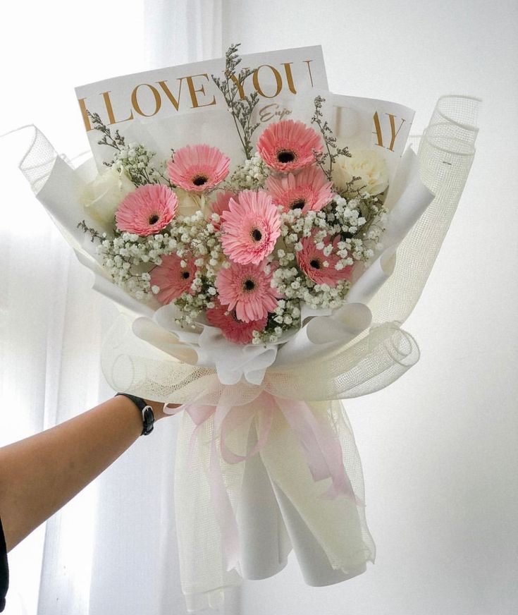 a bouquet of pink and white flowers is being held by a woman's hand