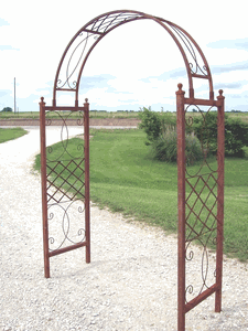 two metal archways sitting on top of a gravel road next to a lush green field