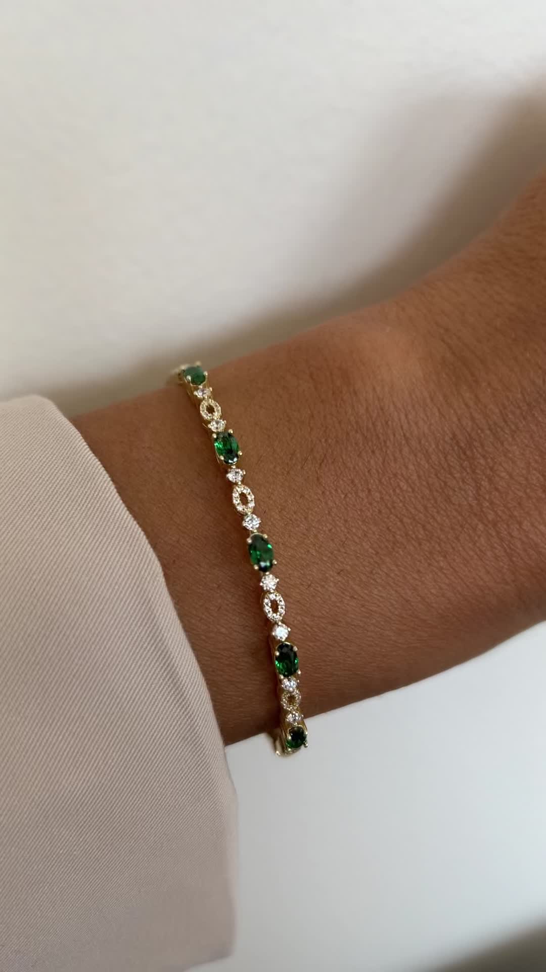 This contains: A video pin of a gold and emerald bangle.