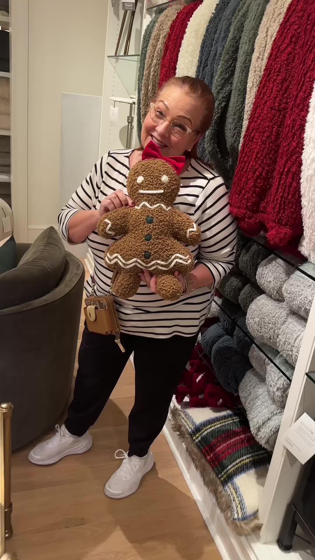 This may contain: a woman holding a teddy bear in front of a rack of sweaters