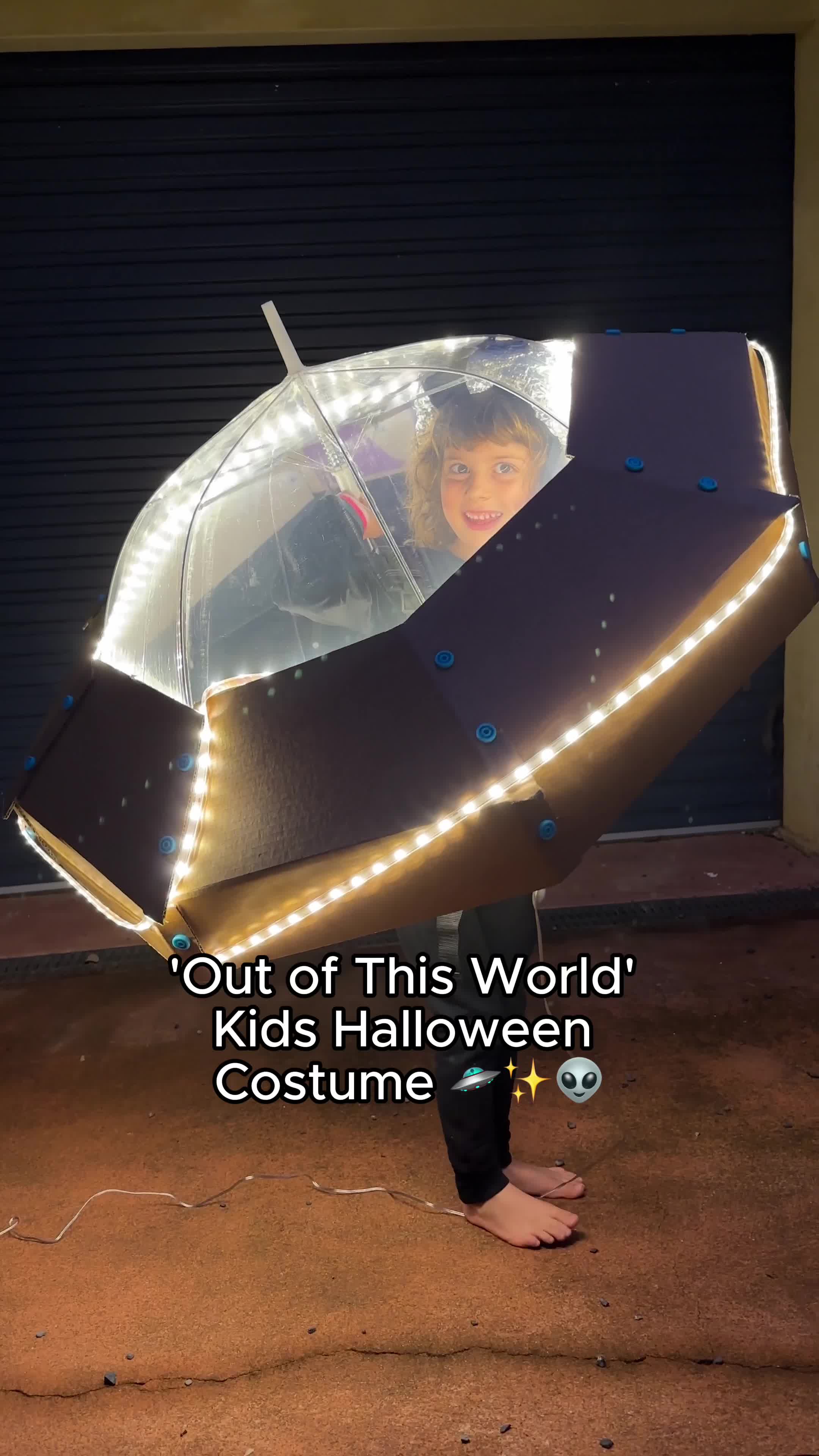 This may contain: a woman holding an umbrella with lights on it and the caption out of this world kids halloween costume