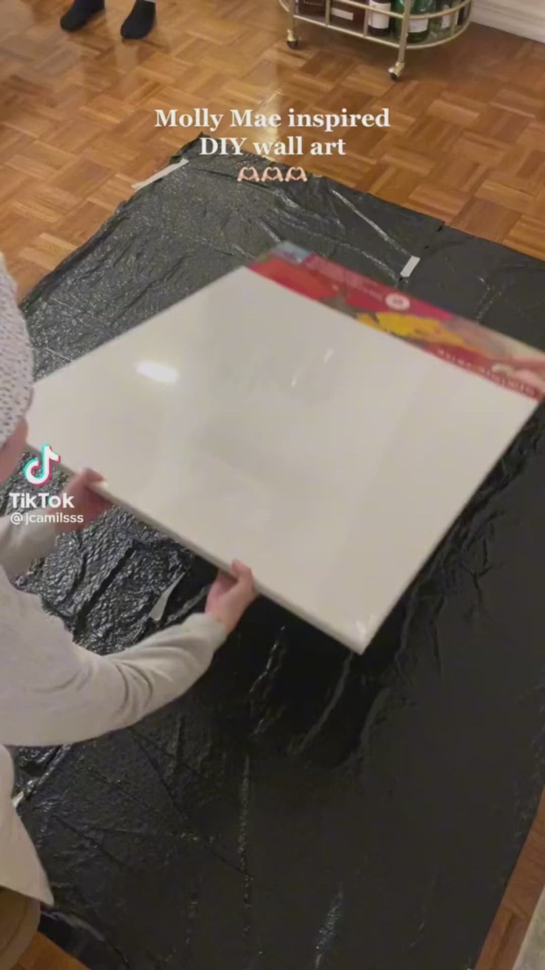 This may contain: a woman is painting a large white piece of art on the floor with black tarp