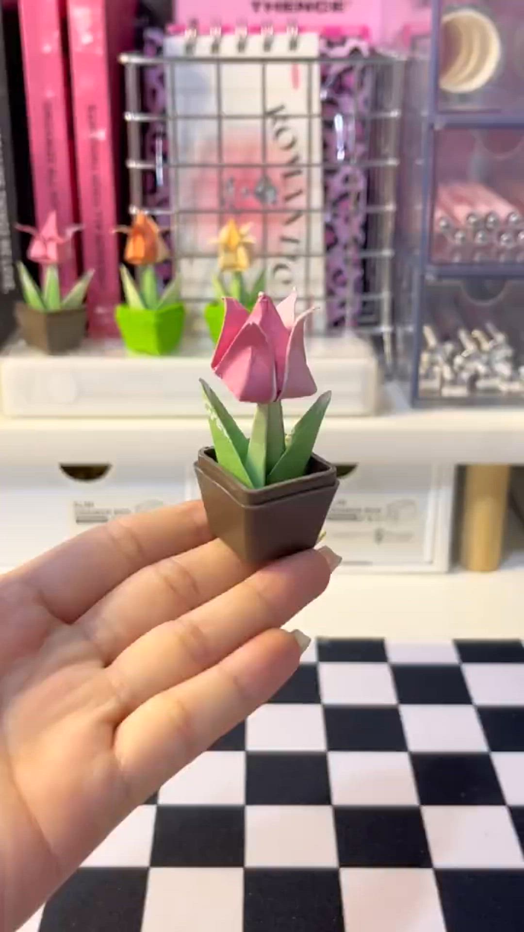 This may contain: a hand holding a small potted plant on top of a checkered countertop