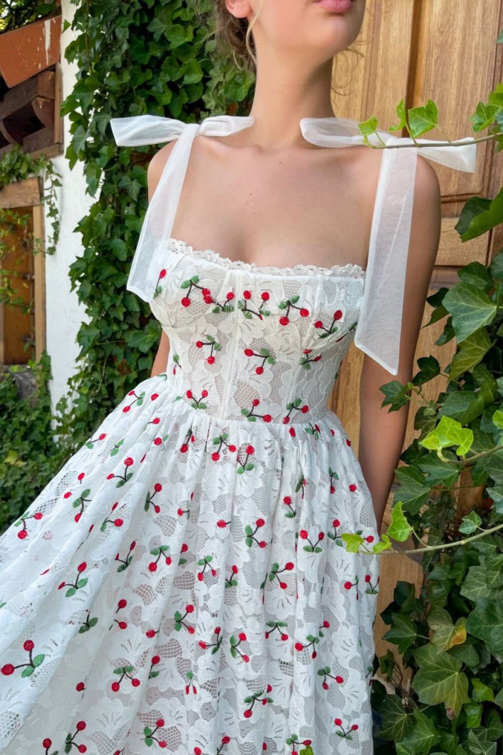 This beautiful Leavers lace fabric features softly embellished cherries in a White Ivory color. The romantic sweetheart neckline is accented with bust cup detail. The corset has built-in pads and boning for a beautiful, tailored look. The midi-length style is elevated with inseam pockets and decorative bow straps.