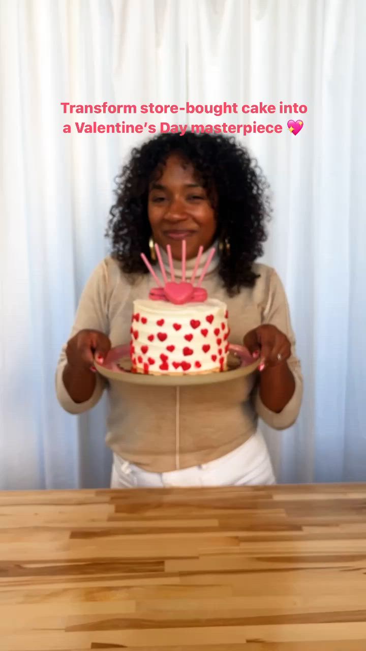 This may contain: a woman holding a cake with candles in her hands and the words transform store bought cake into a valentine's day masterpiece