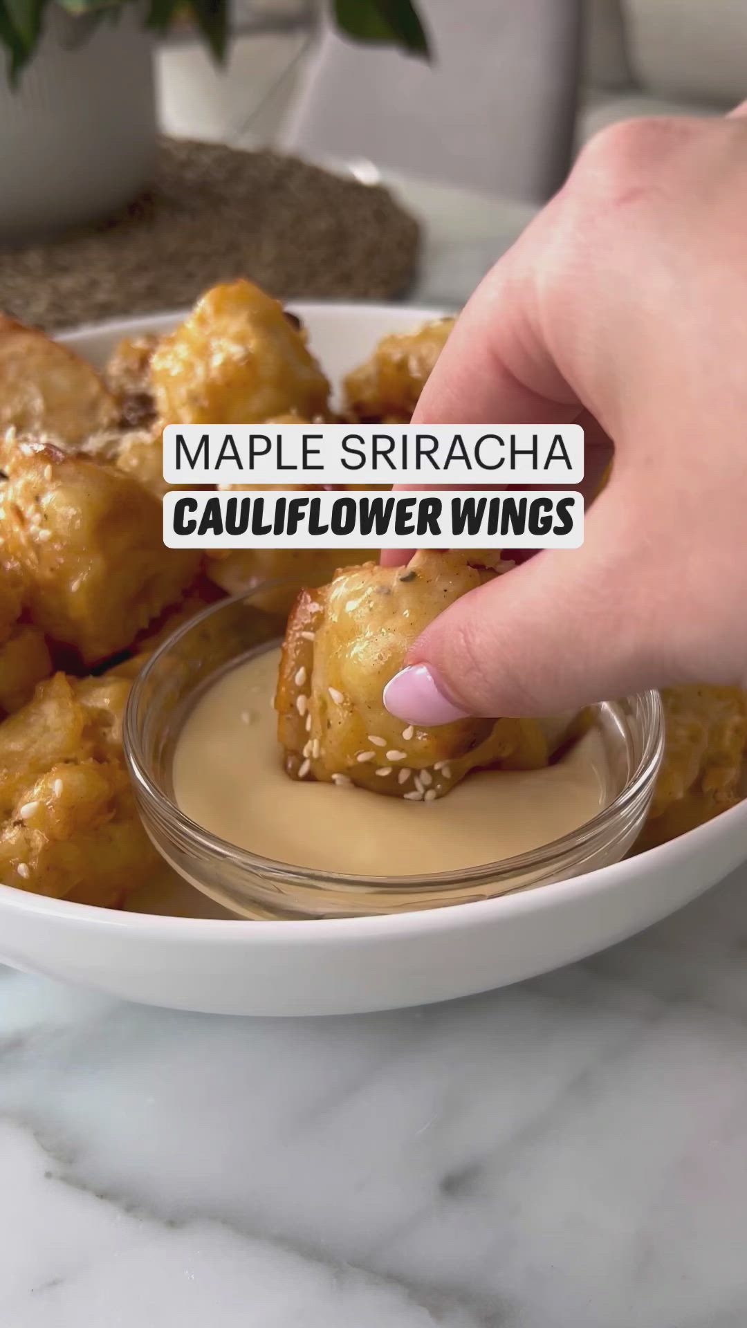 This may contain: a person is dipping some food into a bowl with sauce on the side and another hand holding a sticker that reads maple sricha cauliflower wings