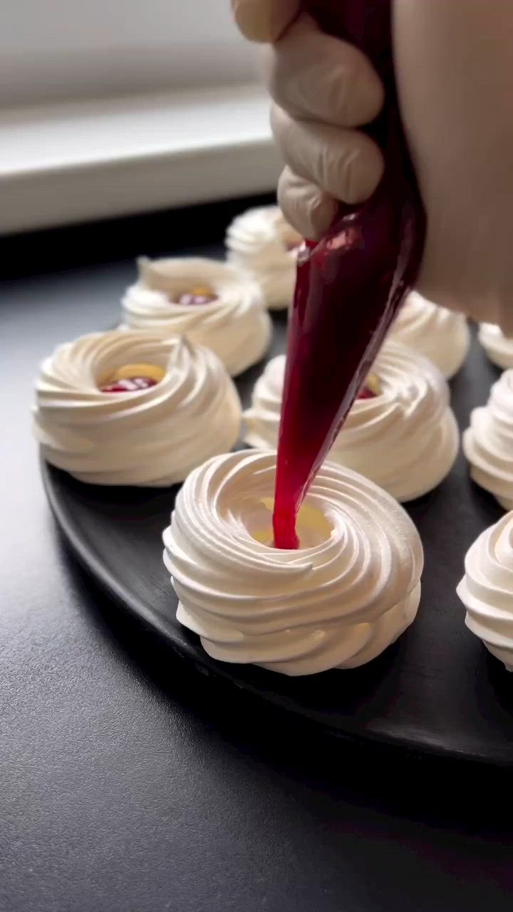 This may contain: someone is decorating small cupcakes with white icing on a black plate