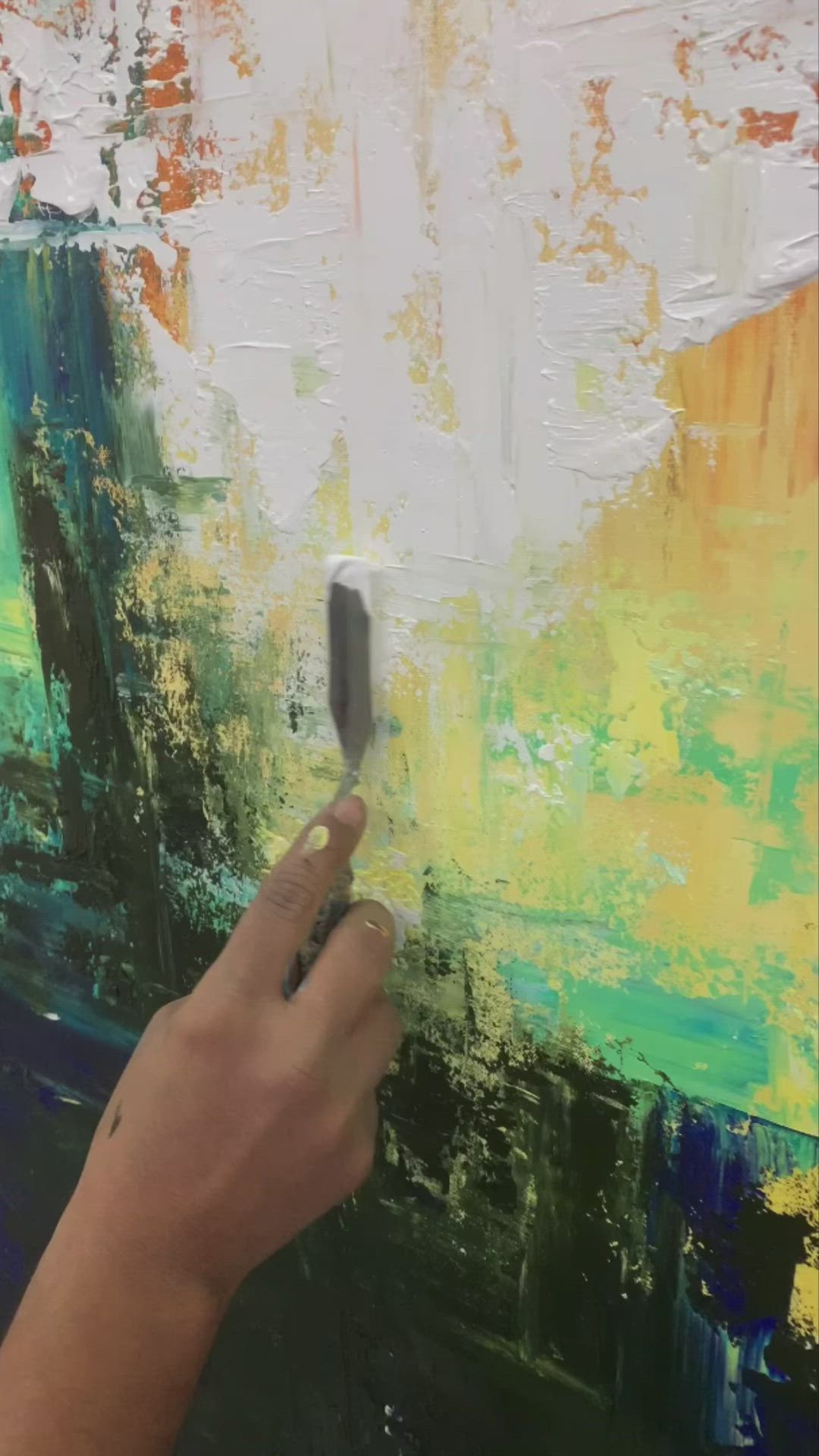 This may contain: a person is painting on an easel with white paint and green, blue, yellow and orange colors