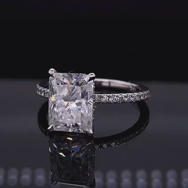 This may contain: an engagement ring with a princess cut diamond surrounded by pave diamonds on a black surface