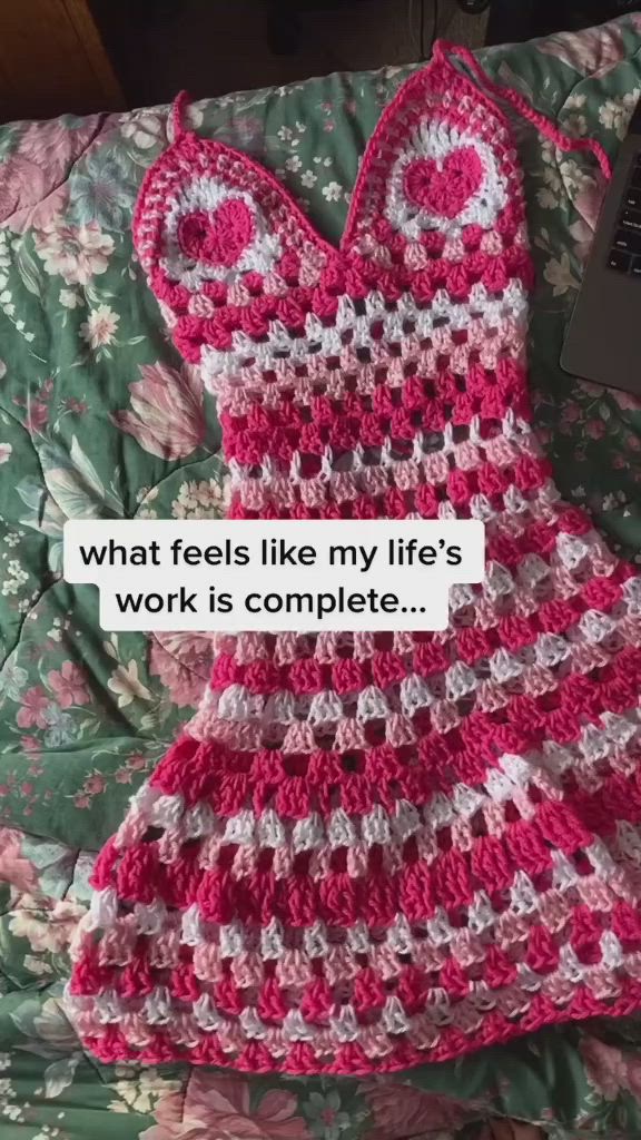 This may contain: a crocheted dress sitting on top of a bed next to a laptop computer