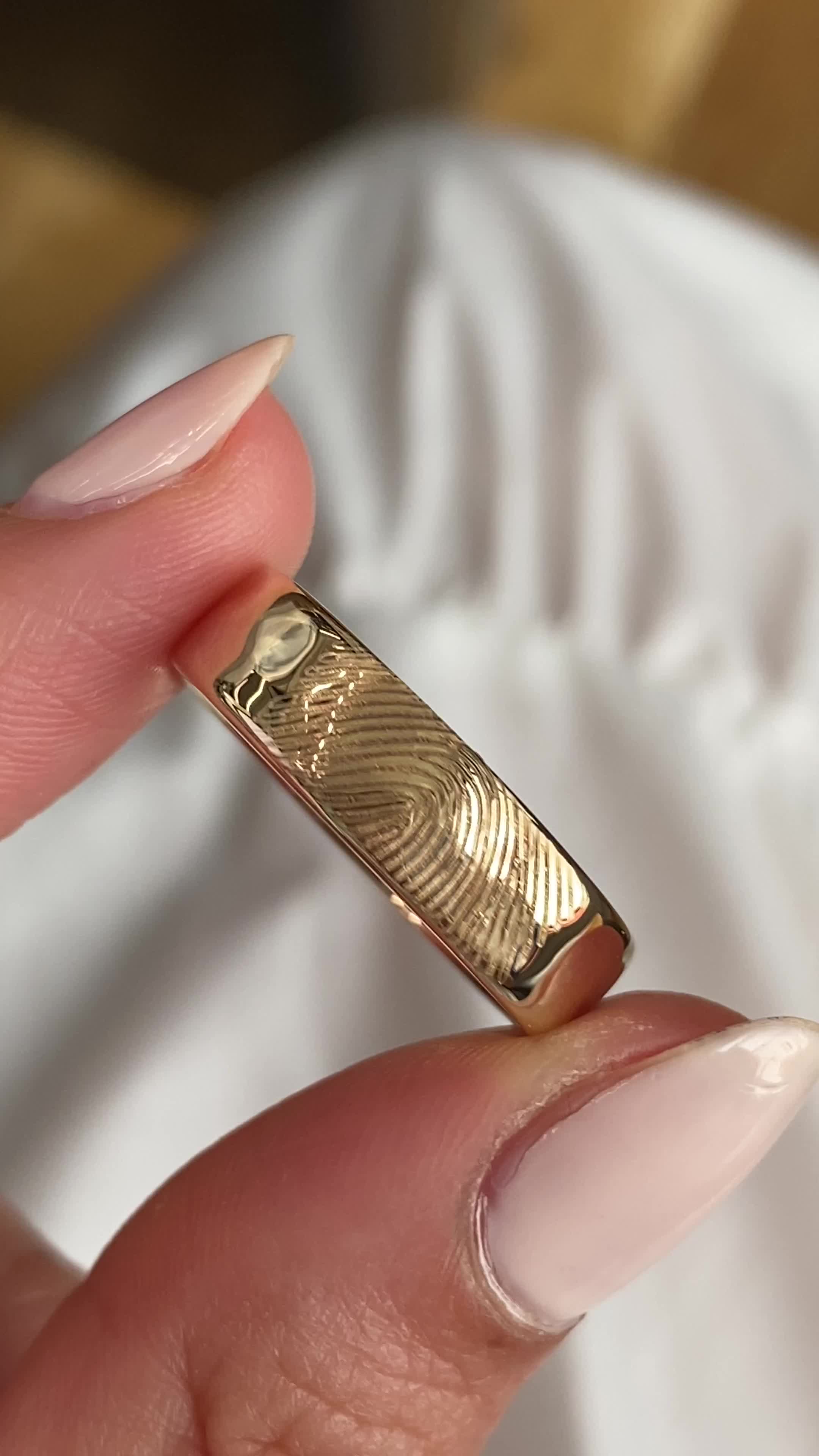 This may contain: a woman's hand holding a gold ring with fingerprints on the side