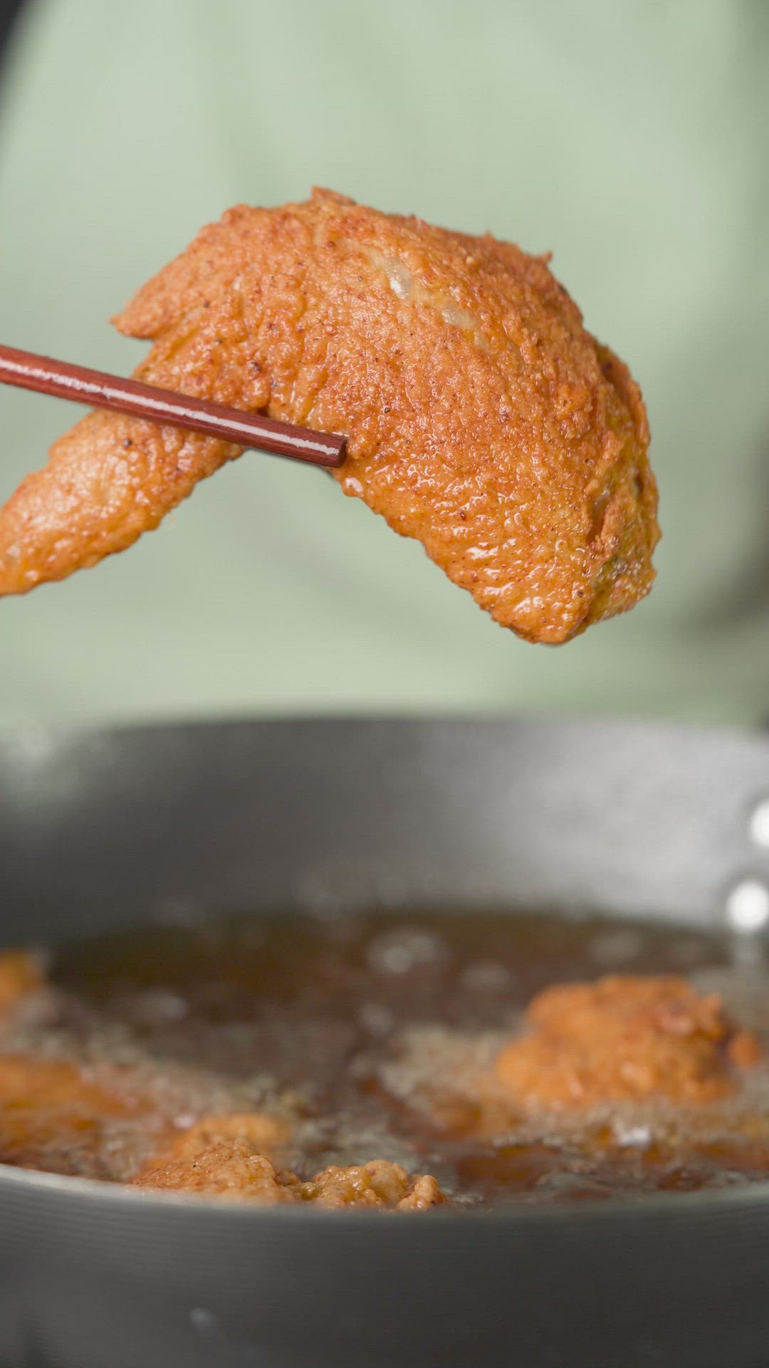 This may contain: a fried chicken wing being dipped with chopsticks in a frying pan filled with broth