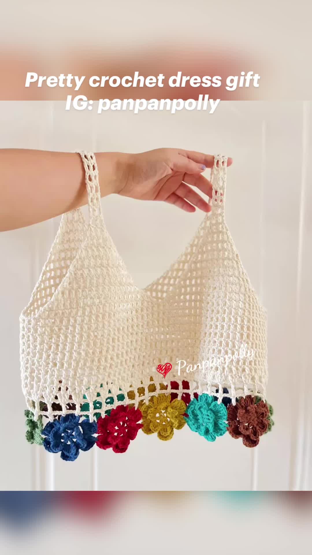 This may contain: a woman's hand holding a white bag with colorful crochet flowers on it