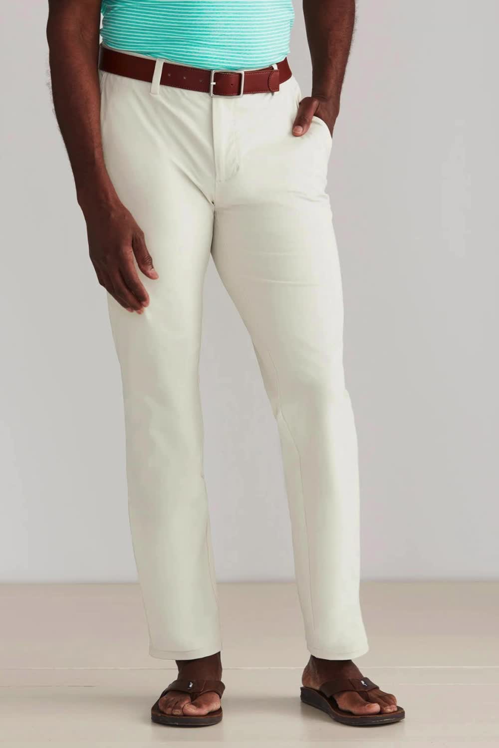 This contains: Man standing wearing white pants with a brown belt