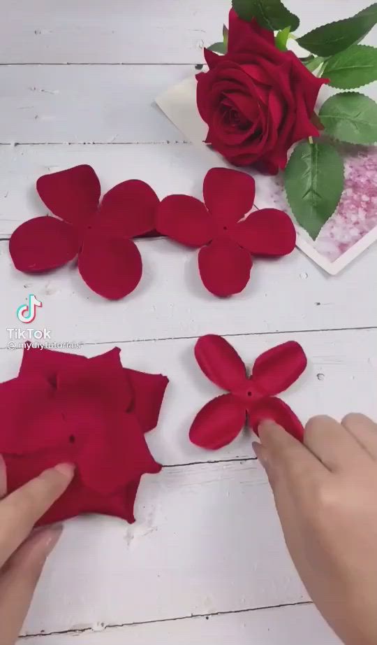 This may contain: a close up of a red rose on a white table with green leaves and flowers